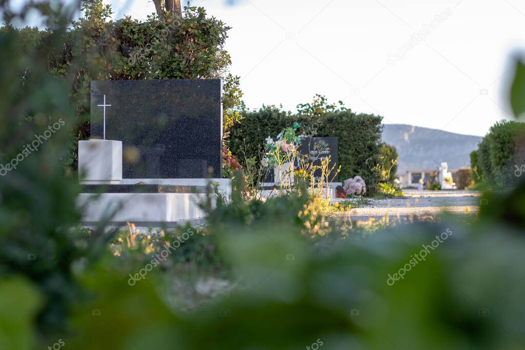 Blank grey granite tombstone with a white christian cross. Sunny bright day, graveyard