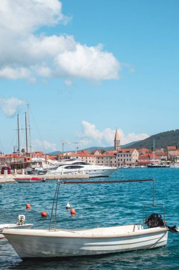 Starigrad 'ın sahil manzarası dikey, Hvar. Ön taraftaki eski tekneler rıhtıma yanaştı, evler ve uzaktan görülen ünlü kilise çan kulesi.