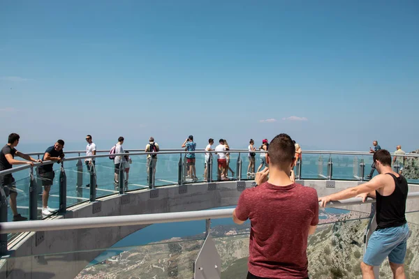 Biokovo dağında yeni inşa edilen gökyüzünde yürüyen turistler. Ön planda iki adam uzaktan hayranlıkla fotoğraf çekiyor.