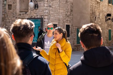 Hırvatistan 'ın SIbenik kentinde sarı ceketli bir grup yolcuyla konuşan kadın turist rehberi