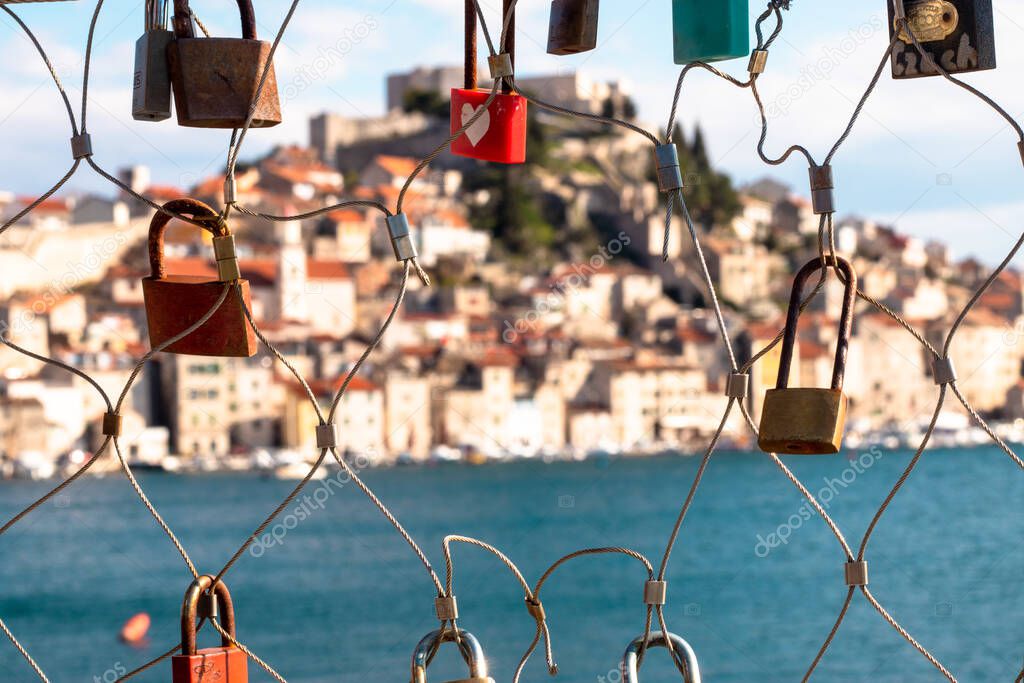 Chain of love lockets with a hole in it in Sibenik Croatia. Blue sea and old town center in the distance