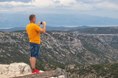 Vidova Gora, Hırvatistan, Ağustos 2020 Vidova Gora dağının kenarında duran ve akıllı telefonuyla fotoğraf çeken turist. Popüler seyahat ve yürüyüş rotası