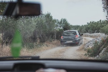 Hırvatistan 'ın Brac adasındaki toprak yollarda küçük gri bir hatchback sürüyordu. Küçük yollarda zeytin ağaçları ve kayalar arasında gidip geliyordu. Arkasına da toz atıyordu. Onu takip eden arabadan görüldü.