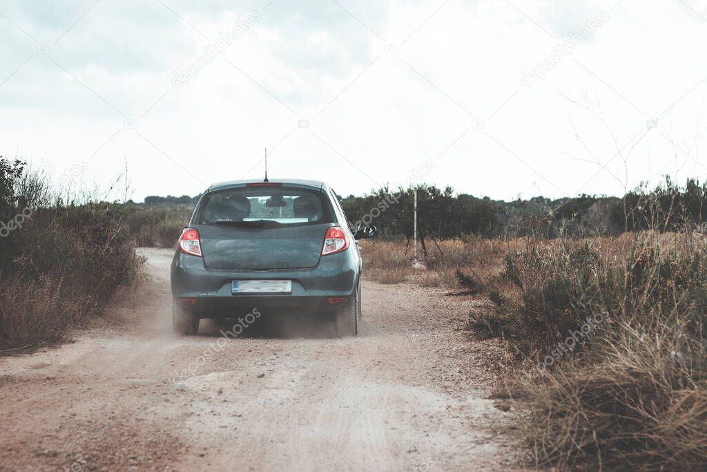Small grey hatchback driving on dirt roads on the island of Brac, Croatia. Driving between olive trees and rocks on small paths, throwing dust behind it. Seen from the car behind following it