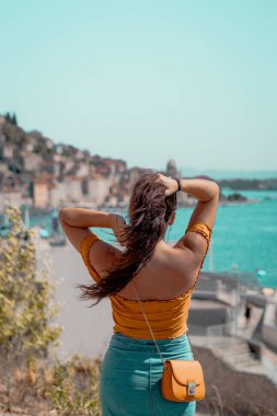 Çekici bir esmer kadının uzun saçlarını kaldırıp mesafeye baktığı arka plan görüntüsü. Açık mavi deniz kenarında poz veren Hırvatistan 'ın Sibenik kentinin ana hatları