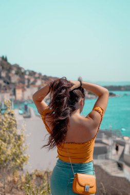 Çekici bir esmer kadının uzun saçlarını kaldırıp mesafeye baktığı arka plan görüntüsü. Açık mavi deniz kenarında poz veren Hırvatistan 'ın Sibenik kentinin ana hatları