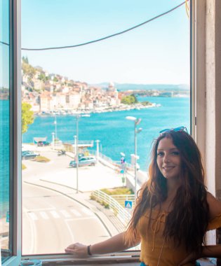 Camın kenarında poz veren ve gülümseyen çekici esmer, kıyı kasabası Sibenik, uzaktan Hırvat. Hırvatistan 'ı ve Adriyatik Denizi' ni gezmek, yaz boyunca olumlu hisler