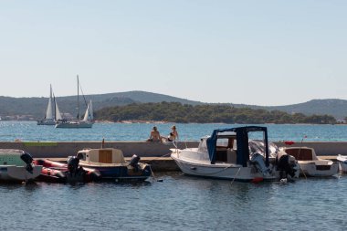 Biyograd Hırvatistan Ağustos 2020 'de Biograd' ın taş limanına yanaşan küçük balıkçı tekneleri, duvarda oturan ve güneşlenen kadınlar. Denizde basit, ılık bir yaz günü