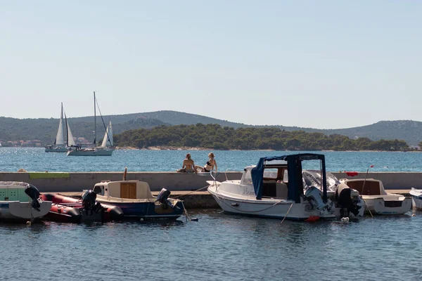 Biyograd Hırvatistan Ağustos 2020 'de Biograd' ın taş limanına yanaşan küçük balıkçı tekneleri, duvarda oturan ve güneşlenen kadınlar. Denizde basit, ılık bir yaz günü