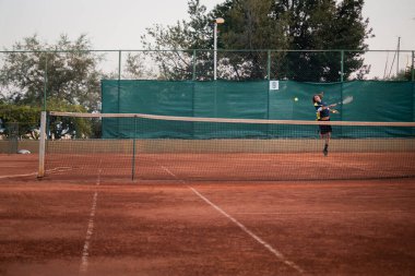 Hırvatistan 'ı Eylül 2020' de turuncu toprak bir tenis sahasının geniş açısıyla ikiye böl, diğer taraftaki adam kameraya doğru uçan topa vurmak için dönüyor