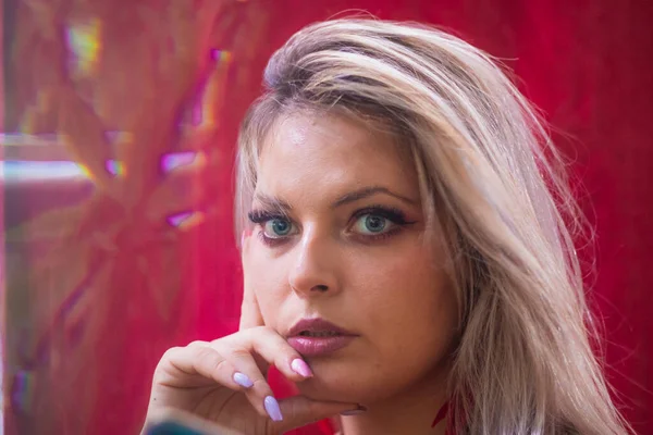 Çekici bir sarışının, ellerini yanağına dayayıp kameranın arkasına baktığı yakın plan. Merceğin önündeki cam prizma renkli şekiller ve etkiler yaratıyor.