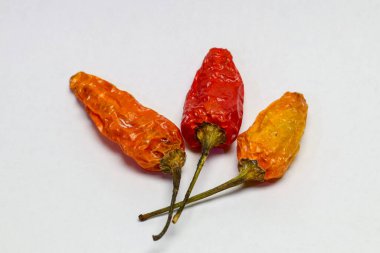 Beyaz arka planda üç kuru kırmızı kuş gözü biberi.