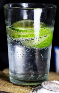 Bir bardak soda ve limon dilimleri koyu bir arka planda.