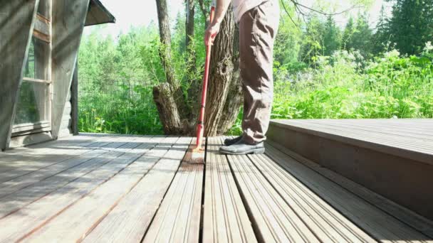 Un hombre caucásico, de 45-50 años, lleva un pincel en la mano. Pintor pinta una terraza de madera. — Vídeo de stock