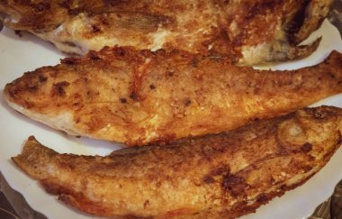 Beyaz bir tabakta üç orta pişmiş balık.