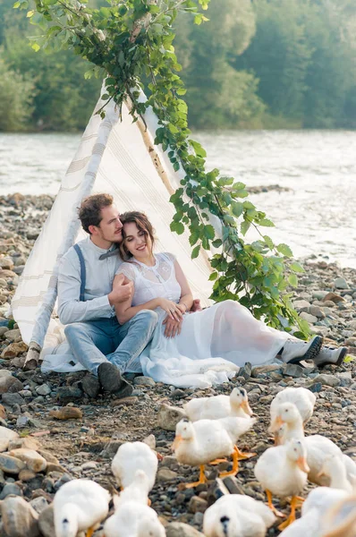 新郎と新婦の山背景の結婚式のアーチの近くの山の湖の海岸に座っています 石の山の川の岸にアヒルの結婚式のカップルを供給 — ストック写真