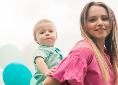 Anne ve küçük oğlu güneşli gün parkta geçirmek. Çekici anne sevimli çocuk, açık havada, closeup tutar. Anne oğlunu sırtlama üzerinde taşıyan.