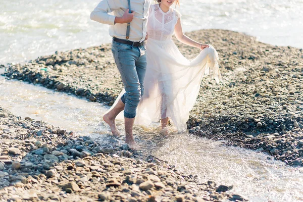 幸せな 感情的な豪華なスタイリッシュな新郎新婦楽しんで 水の飛沫 素足で山川に沿って実行している結婚式のカップル — ストック写真