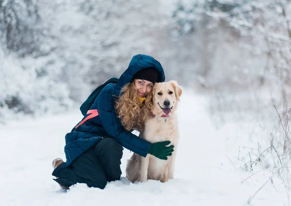 Young beautiful woman hugging golden retriever dog in winter forest — Stock Photo, Image