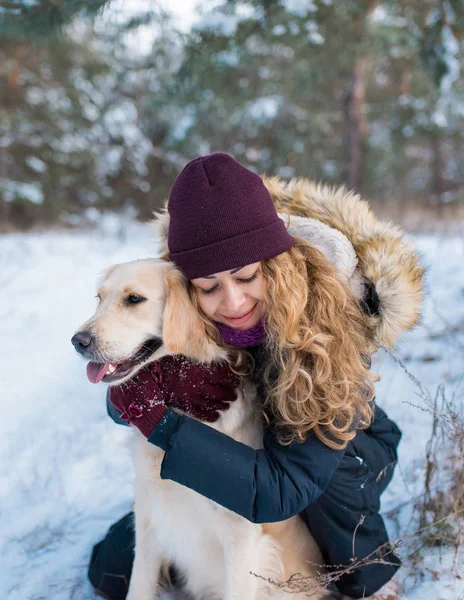 Oung beautiful woman hugging golden retriever dog in snow — Stock Photo, Image