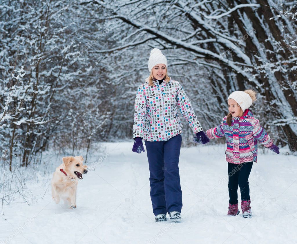 Cheerful mom and her cute daughter with their dog golden retriever in winter