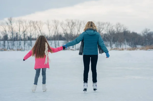 Mladá rodina se bavit na ledové plochy v zasněženém parku — Stock fotografie