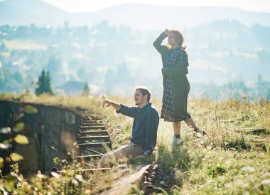 Güzel güzel sevimli iki kişi, şık adam ve rahat kıyafetler giyen modern kız portresi. Sabah güneşi dağlardaki eski demiryolu üzerinde duran kadın ve erkek. Yaşam tarzı lovestory