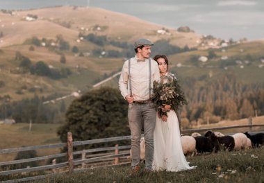 Beyaz elbiseli gelin ve damat takım koyunları mera üzerinde Romantik Çift düğün genç. Düğün yürüyüş doğa hills arka planda. Koyun için mükemmel mera