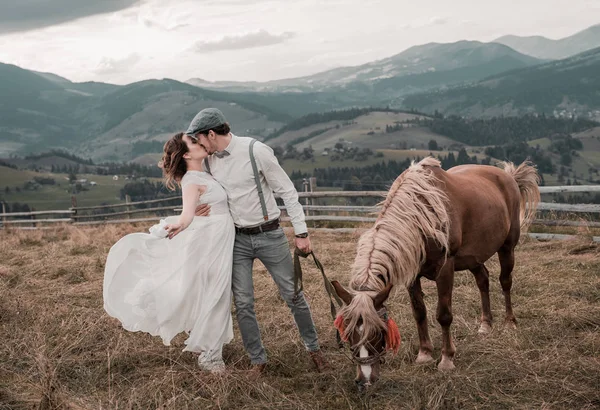 山の岩で新郎新婦のウェディング 山の中腹のカップルのキス 山の背景に馬で服を結婚式の新郎新婦 — ストック写真