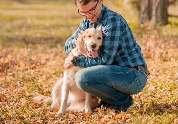 Mladý muž, který na podzim objímal zlatého psa extraktoru — Stock fotografie
