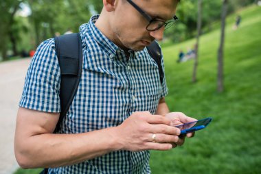 yakışıklı adam çim açık havada oturan ve akıllı telefon kullanarak