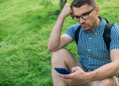 yakışıklı adam çim açık havada oturan ve akıllı telefon kullanarak