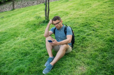 Yakışıklı öğrenci çim üzerinde smartfone ile oturan