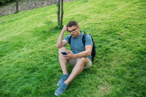 Yakışıklı öğrenci çim üzerinde smartfone ile oturan