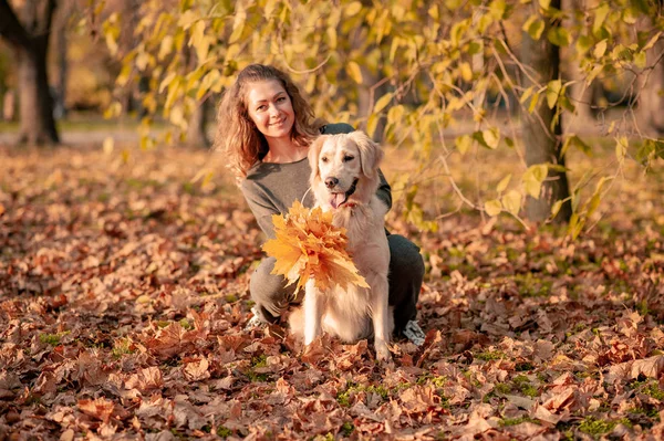 Gros plan de la femme bouclée assise avec son chien dans les feuilles d'automne à l'extérieur — Photo