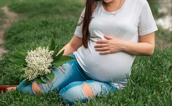孕妇的衣服 穿着白色T恤 手里拿着外面山谷里的一束百合花 怀孕的女人抱着肚子 — 图库照片
