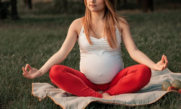 Young pregnant woman meditating in nature, practice yoga. Pregnancy, sport and health lifestyle - young pregnant woman. Care of health and pregnancy