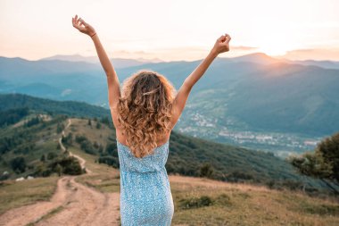Kıvırcık kadın mutlu bir şekilde gülümsüyor yaz tatillerinde kollarını kaldırıp dans ediyor..