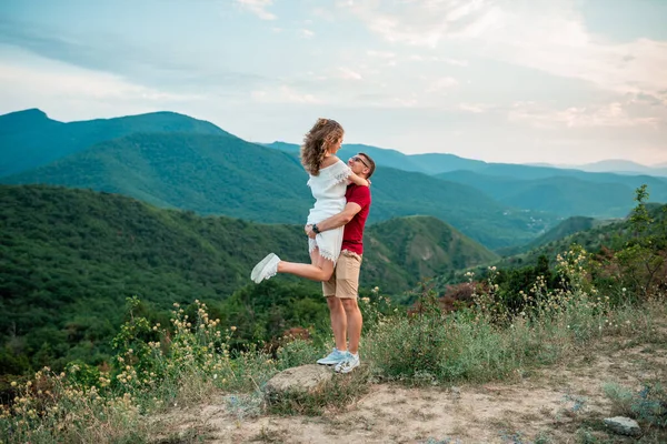 Pareja joven camina en la naturaleza en las montañas tomados de la mano y mirando el uno al otro —  Fotos de Stock