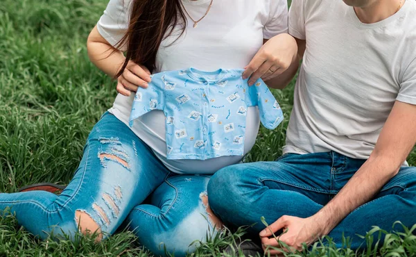 在绿地上 孕妇和丈夫一起抱着婴儿衣服的剪影 真诚的温柔时刻 — 图库照片