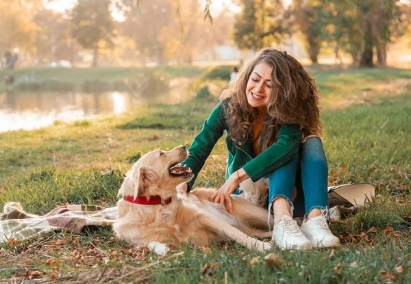 Happy woman together with golden retriever dog in a park outdoors. Young female owner hugging pet in park on brown blanket plaid. love and care for the pet.