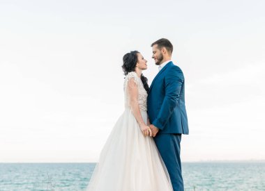 Güzel bir düğün çifti, damat ve gelin, deniz kıyısında yürüyor, koşuyor, gülüyor, eğleniyorlar. Düğün istirahatı, rahatlama balayı konsepti.