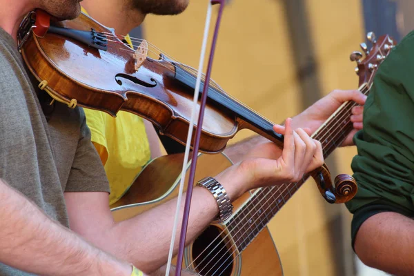 müzisyen ön planda başka bir müzisyen gitar arka planda çalmaya ile keman çalıyor