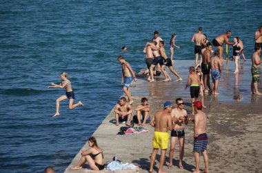 Gençler ve gençler beton iskelede güneşlenir ve banyo yaparlar. 