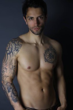 Seksi erkek model gri arka plan üzerinde üstsüz poz. Yakışıklı dövmeli adam 