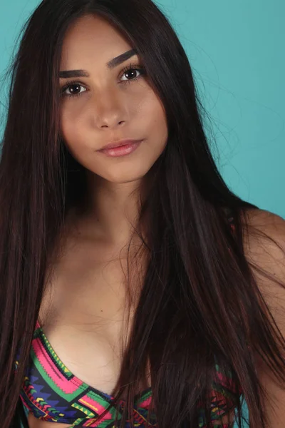 Young beautiful tanned woman in swimsuit posing against blue background. Closeup Fashion portrait of beautiful girl with long straight brunette hair.
