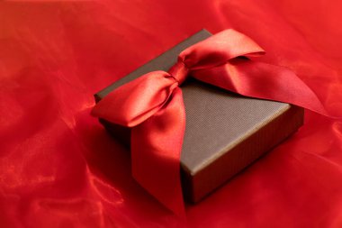 Kırmızı arka planda saten fiyonklu Noel hediyesi kutusu.