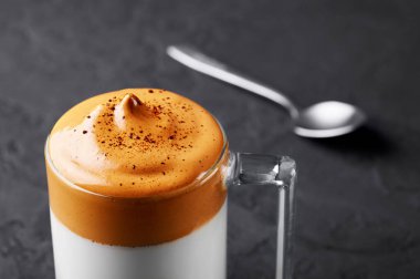 Dalgona Kahve, şeffaf bir fincanda, siyah tahta masa üstünde. Dalgona Köpüklü Kahve, kremşantili kahve, şeker ve süt içeren bir Güney Kore içeceğidir..