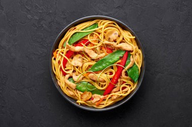 Piliç Lo Mein siyah kasede, arka planda. Lo Mein, tavuk eti, erişte, sebze ve soslu Çin mutfağı. Çin yemeği. Kızarmış erişteyi karıştır. Uzayı kopyala Üst görünüm