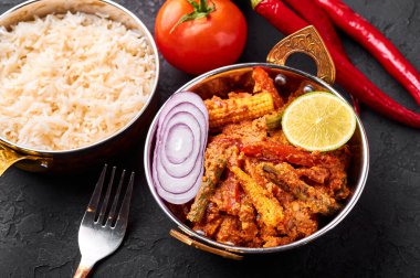 Bakır kadai 'de sebze Jalfrezi ve siyah tahta kaplamalı basmati pilavı. Jalfrezi, Hint mutfağı. Kızarmış sebze ve baharatlı domates sosu. Hint Yemeği.